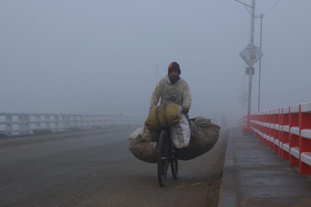 man riding bike with goods inside sack passing through bridge