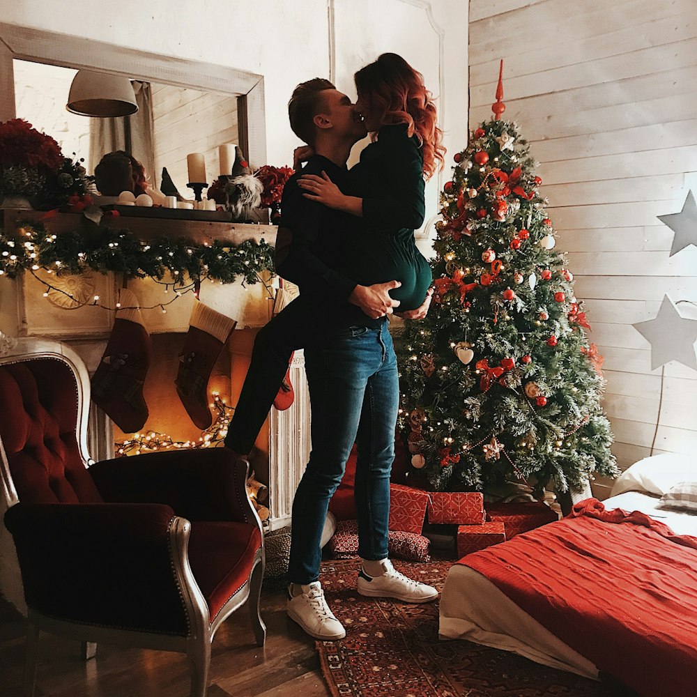 man carrying woman beside green Christmas tree