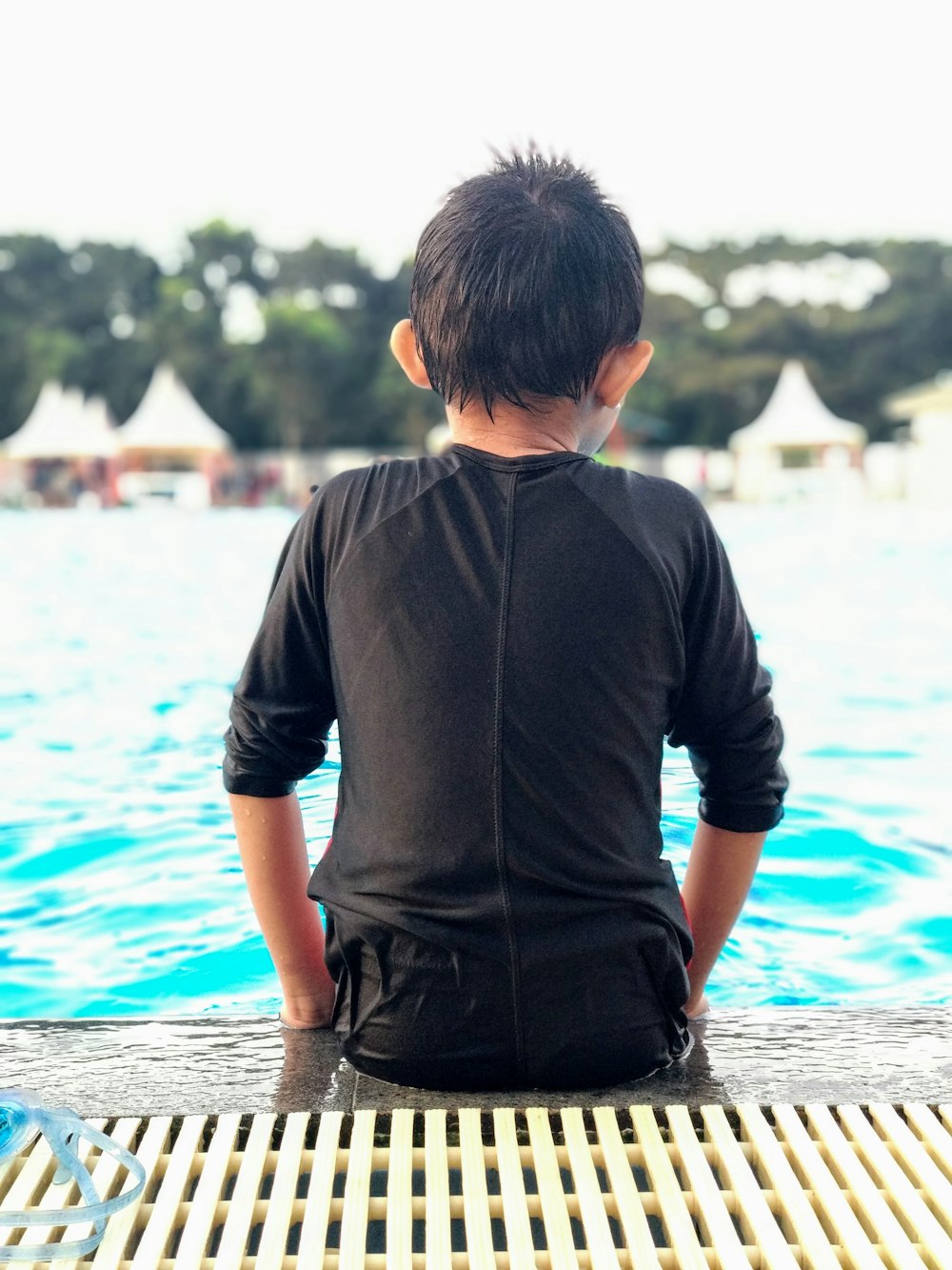 boy wearing black shirt sitting beside pool