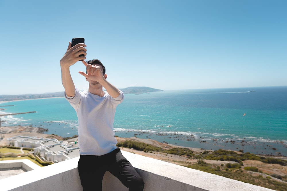 man with smartphone taking self-portrait in balcony overlooking sea