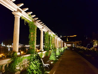 Elegant evening scene of a spacious deck with a pergola, glowing lights, and comfortable seating surrounded by greenery.
