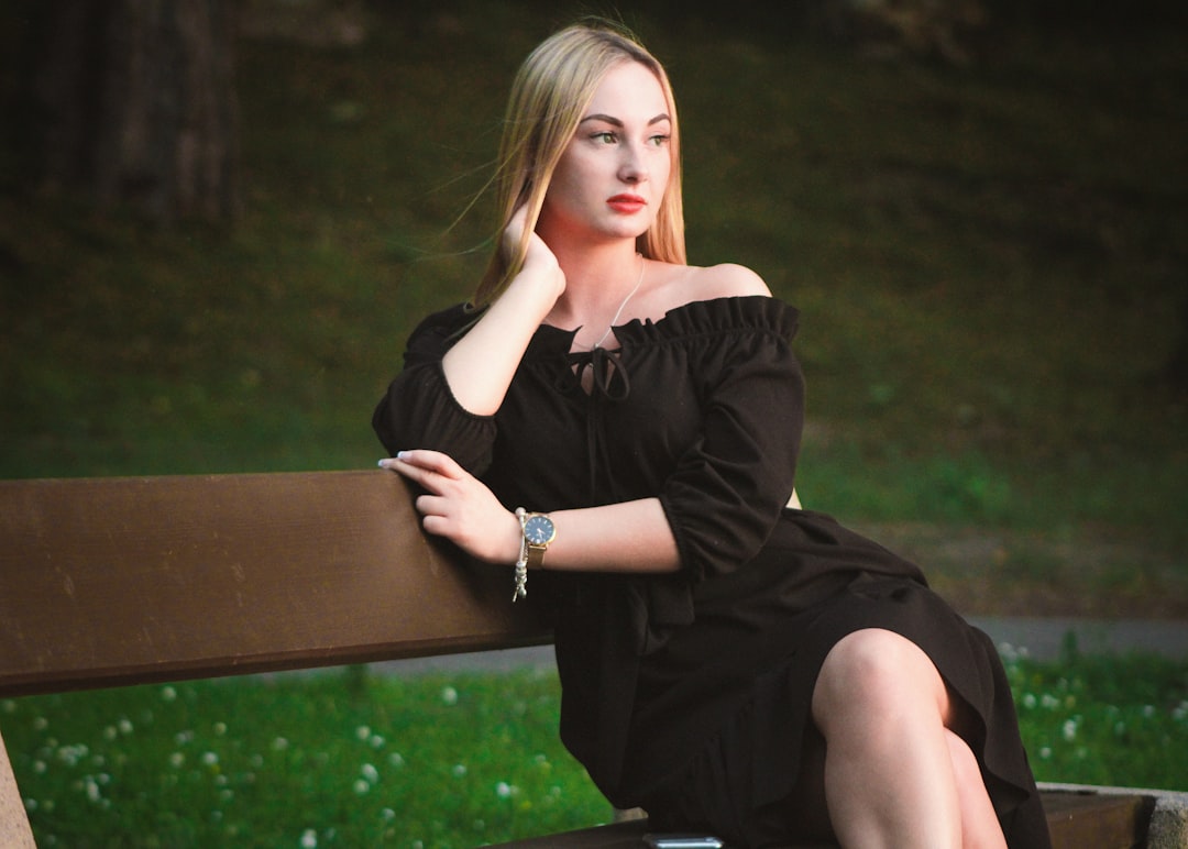woman in black off-shoulder dress sitting on wooden bench