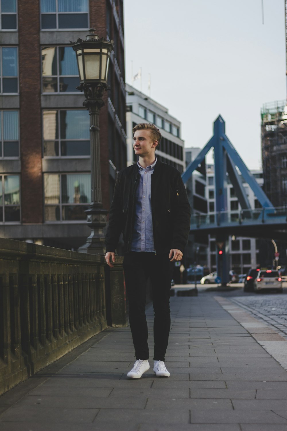 standing man wearing black zip-up jacket standing beside concrete wall