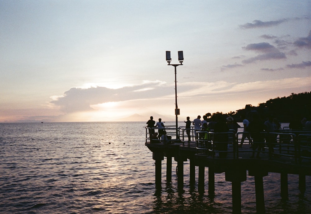 people in dock watching sunset at sea