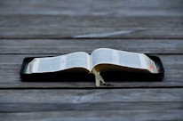 An open book displayed on a wooden surface, with visible tabs and a ribbon marker. The pages contain text in a neatly printed format.