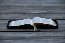 An open book displayed on a wooden surface, with visible tabs and a ribbon marker. The pages contain text in a neatly printed format.