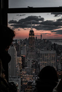 person looking at Empire State Building from glass window at dusk