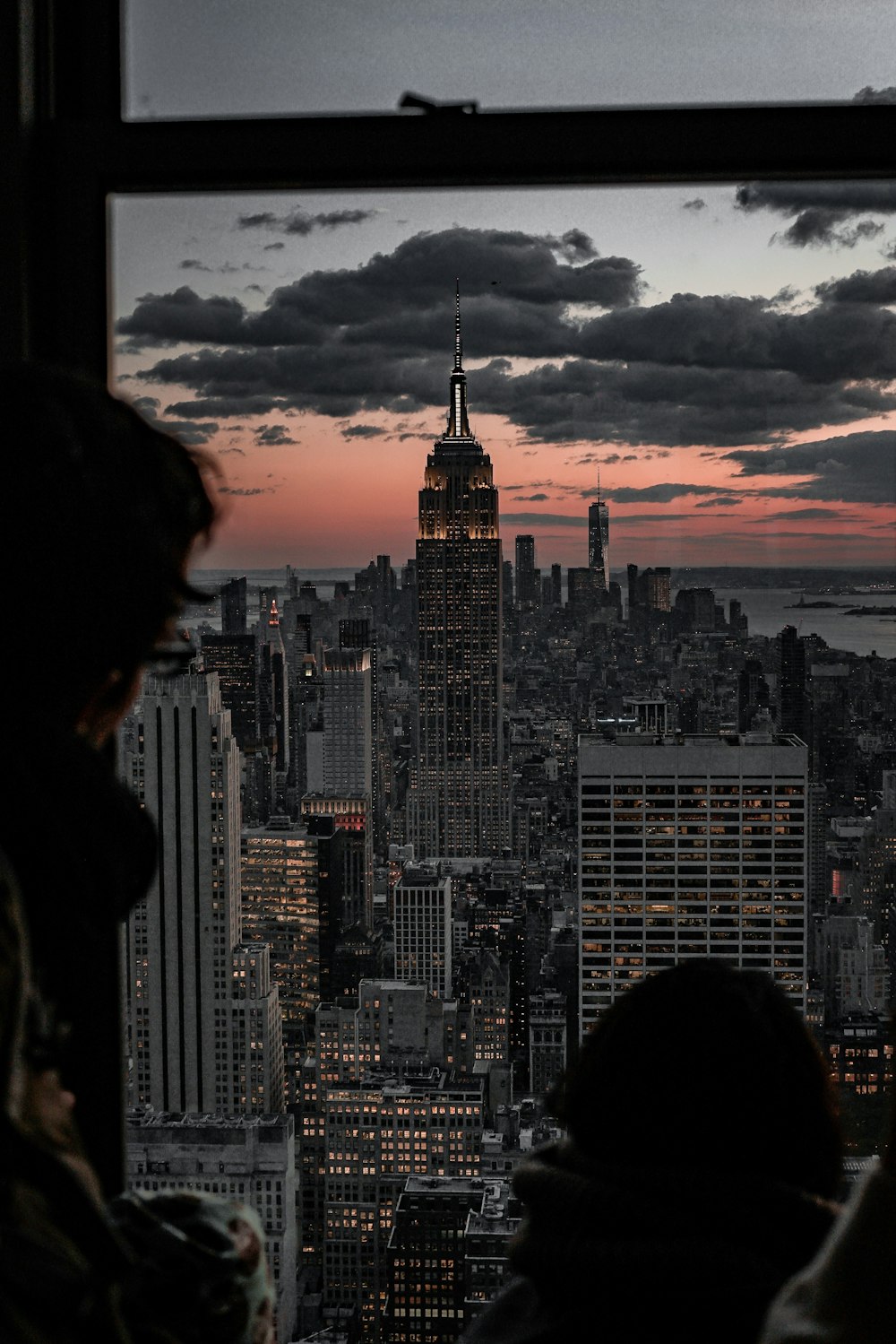 person looking at Empire State Building from glass window at dusk