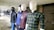Several mannequins are dressed in different casual outfits, displayed in a row inside a retail setting. The mannequins are wearing a variety of clothing items including plaid shirts, leather jackets, and a beanie hat. The background features other mannequins and a partially closed store with a sign.