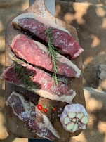 Freshly prepared cuts of goat meat displayed on a wooden board with herbs.