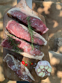 Fresh cuts of premium meat artfully arranged on a dark wooden board with red chili peppers and herbs