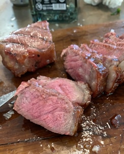 Close-up of juicy ribeye steak cooked medium rare, resting on a wooden board with herbs.