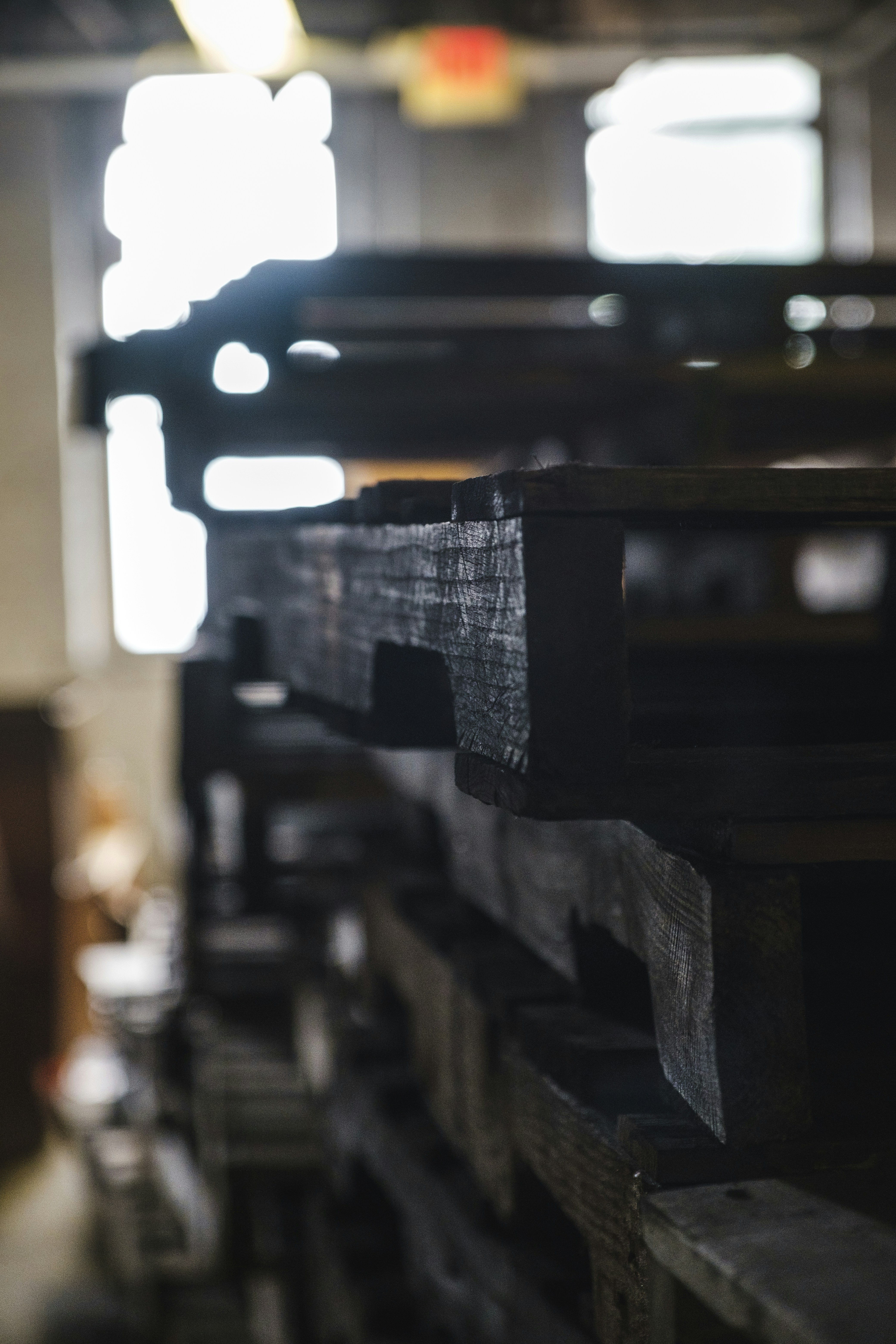 Dimly lit warehouse with stacked wooden furniture, deep shadows, dark atmospheric storage space