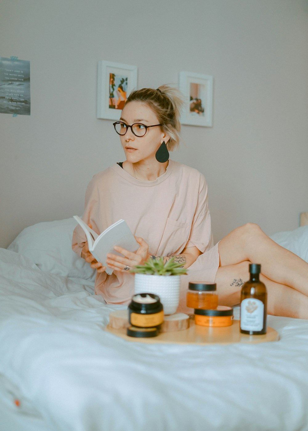 woman holds book on bed near beauty products