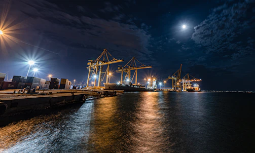 Crane operator guiding a load during a night shift in Uran port area