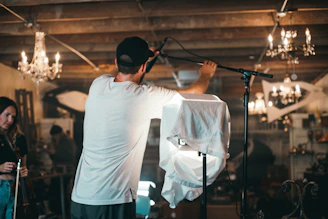 Hands adjusting a microphone on a stand in a cozy underground studio setting.