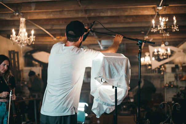 Hands adjusting a microphone on a stand in a cozy underground studio setting.