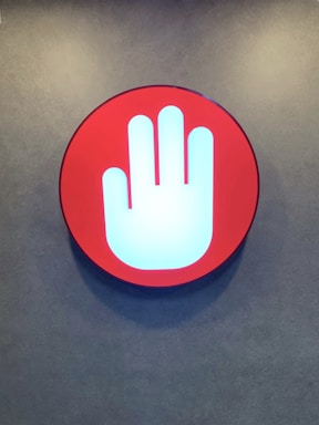 A circular sign featuring a prominent white hand symbol within a red background, mounted against a textured wall.