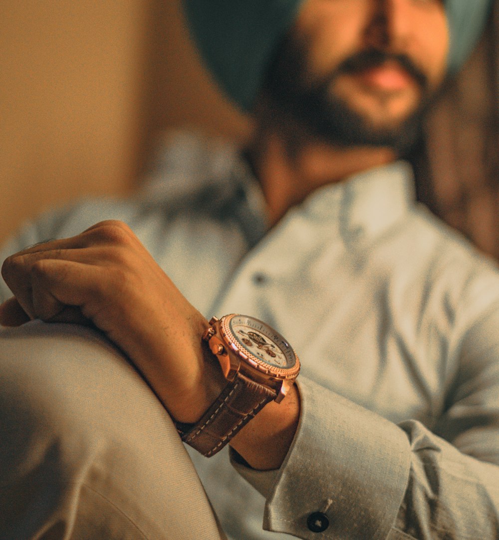 shallow focus photo of man wearing round gold-colored chronograph watch with brown leather strap