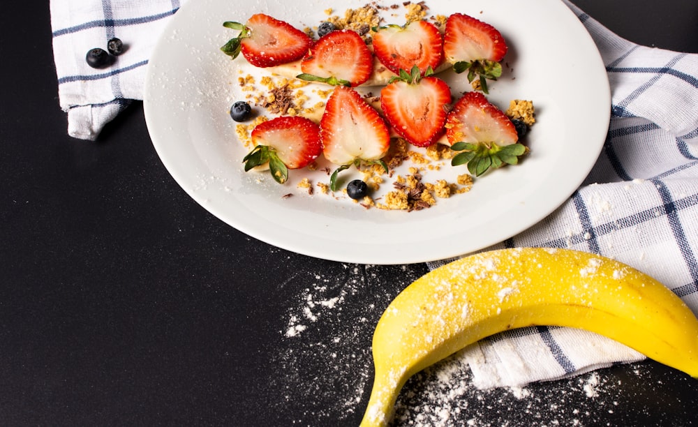 sliced strawberry fruits on plate near one ripe banana fruit