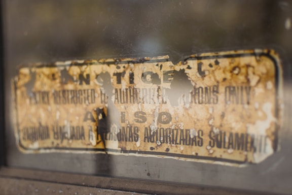 A weathered and old sign partially torn and faded, affixed to a surface with a warning written in both English and Spanish. The text is difficult to read due to the wear and damage on the sign.