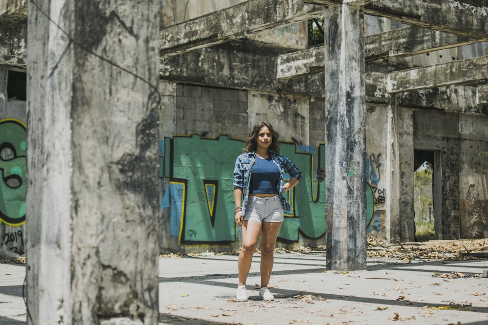 woman in blue shirt, blue plaid blazer and blue denim shorts standing in front of graffiti painted wall