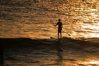 A peaceful sunset view over water with a lone paddle boarder in silhouette.