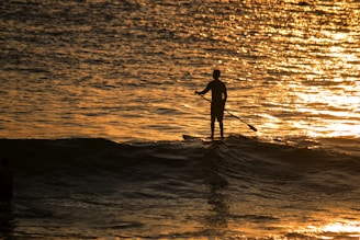 A peaceful sunset view over water with a lone paddle boarder in silhouette.