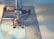A close-up view of a sewing machine needle and presser foot, stitching fabric. The image focuses on the metallic parts of the machine and the blue fabric being sewn, with soft lighting creating a serene ambiance.