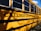 A school bus is parked with the side displaying the words "Chelmsford Public Schools" in bold black letters. The yellow exterior and large windows are visible, casting shadows from nearby trees or surroundings.