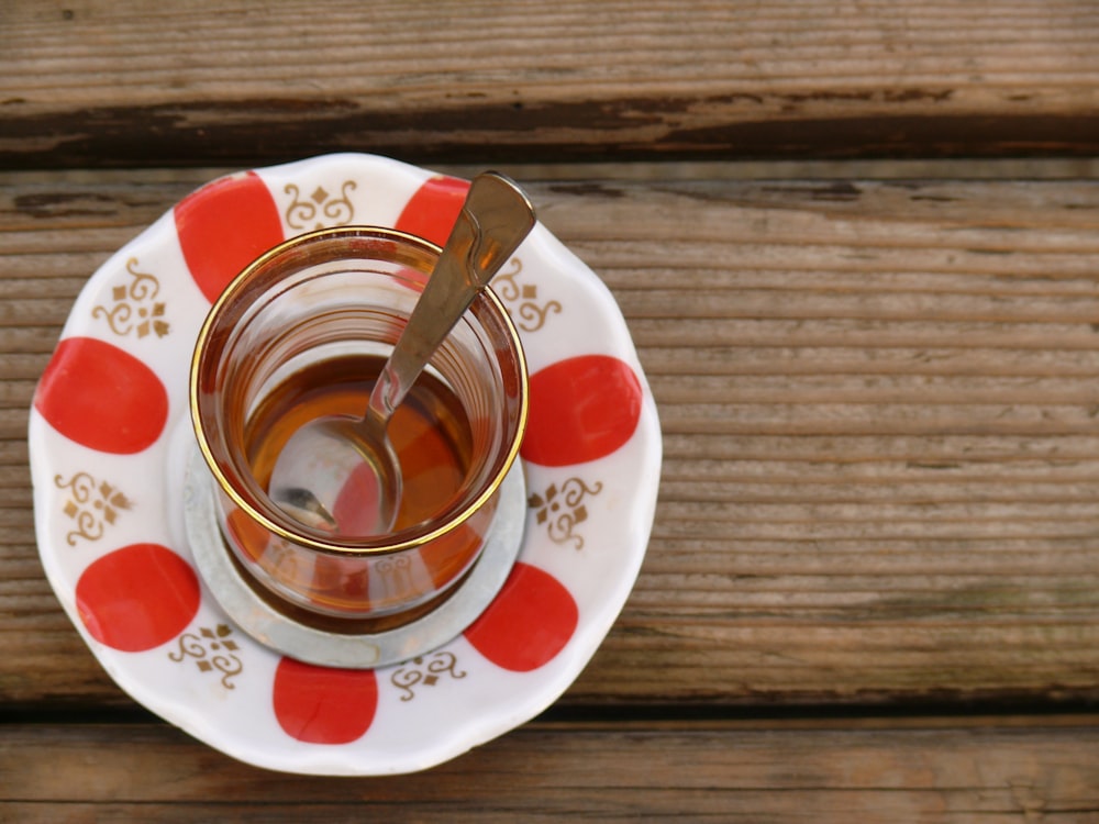 gray spoon in clear teacup on white and red saucer