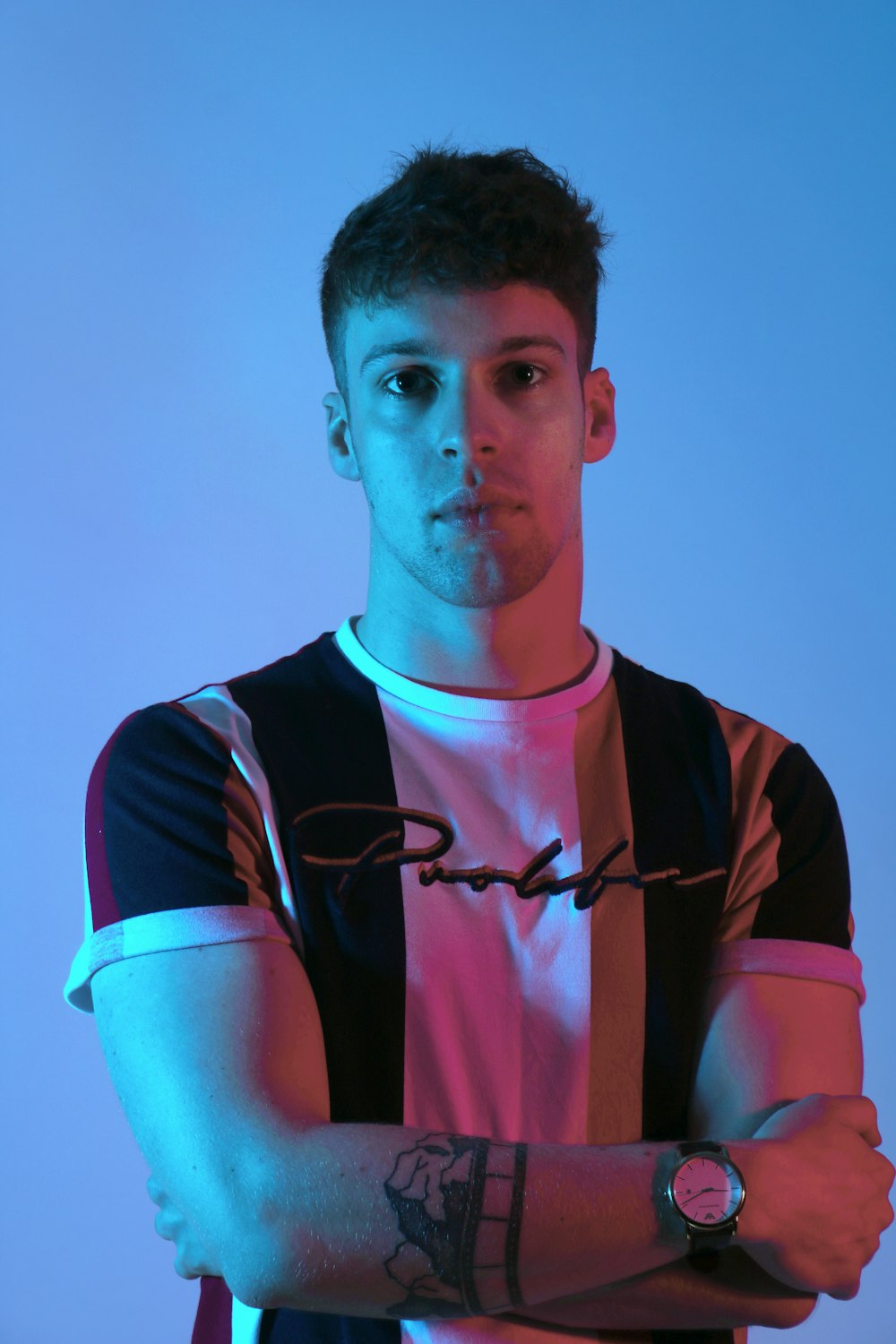 standing man wearing white, brown, and black striped shirt crossed both hands