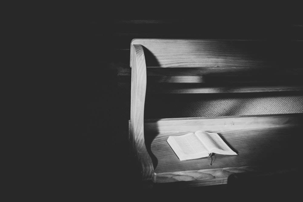 grayscale photo of open book on bench