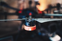 A close-up of a drone rotor with a metallic propeller and an orange base connected to the rotor mechanism. The background is blurred, drawing focus to the intricate details of the drone component.