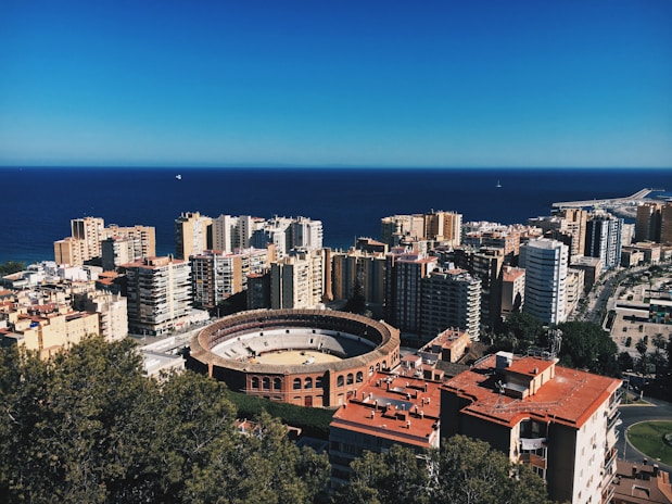 Vista aérea de Málaga con el mar y la plaza de toros, representando oportunidades de inversión VTC