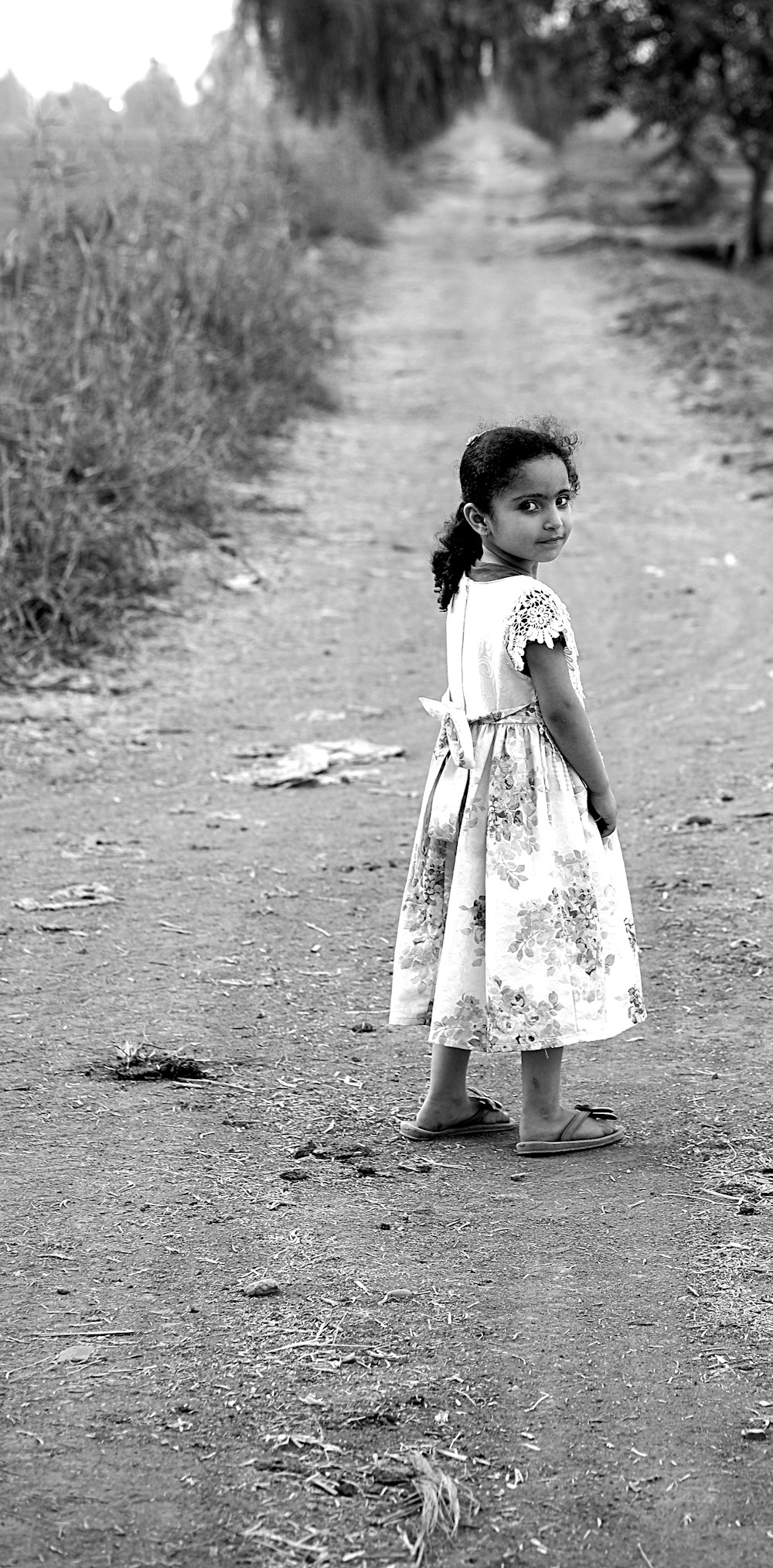 girl standing in the middle of dirt road during day