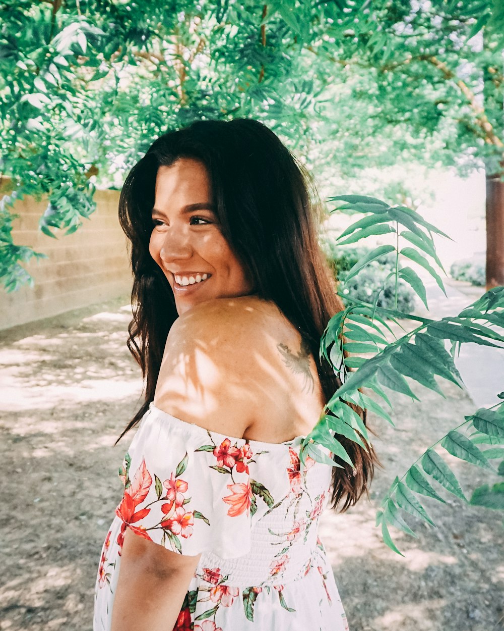 woman in red and white floral dress standing under tree