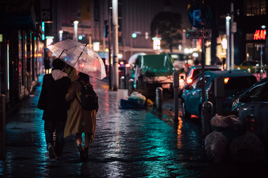 คู่รักกางร่มใสเดินบนถนนโตเกียวที่เปียกฝนยามค่ำคืน