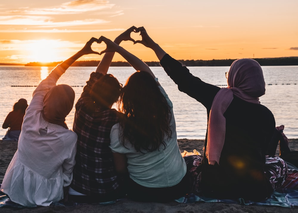 Quatre personnes assises sur le rivage formant des cœurs avec leurs mains pendant l’heure dorée