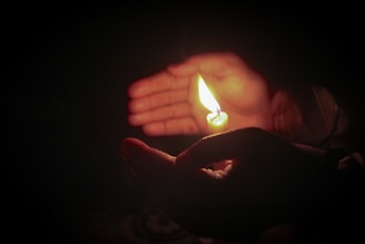 Hands gently holding a lit candle symbolizing care and respect.
