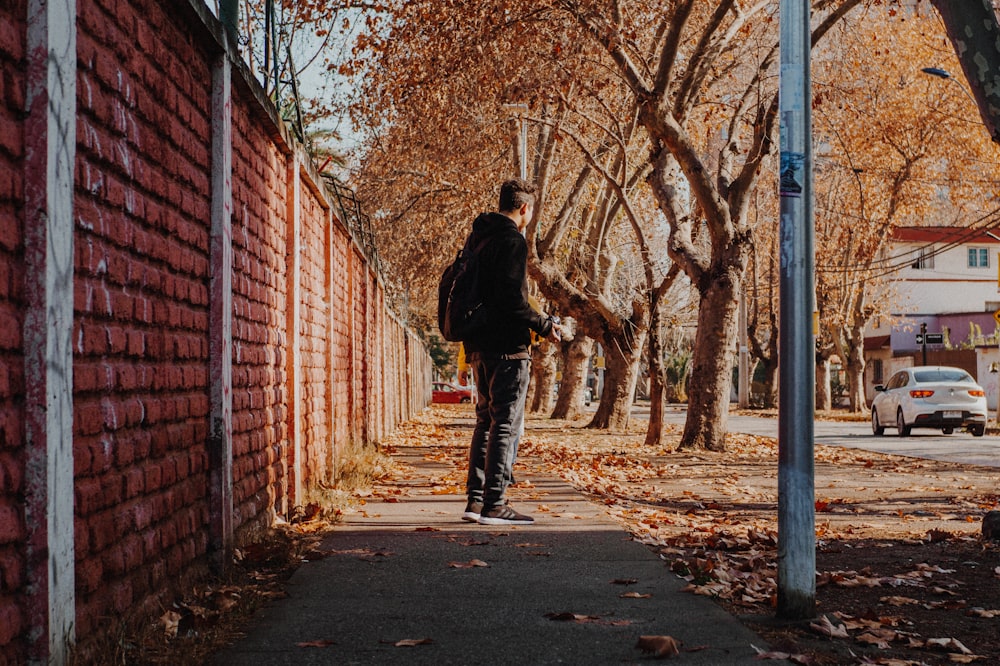 man standing on side walk beside brown trees during daytime