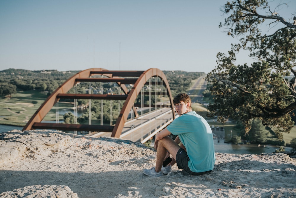 man sitting near the bridge during daytime