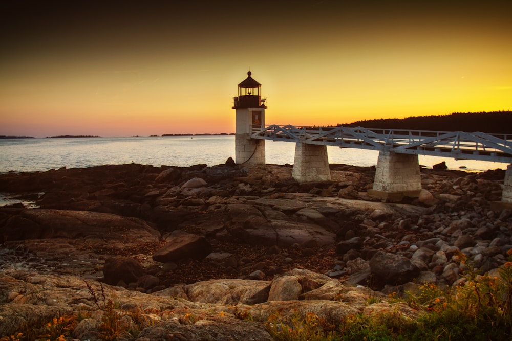 lighthouse with bridge near the ocean during day