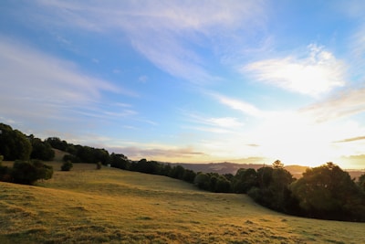 A peaceful rural landscape at sunset with rolling hills and scattered trees.