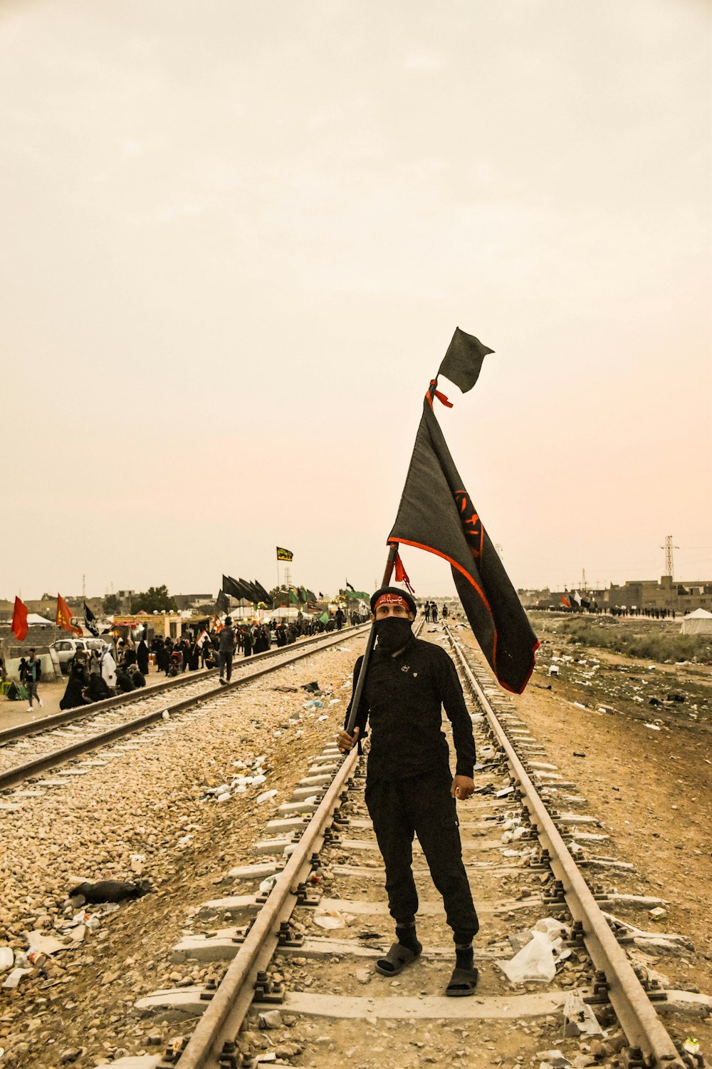 hombre con pasamontañas y bandera de pie en medio de las vías del tren