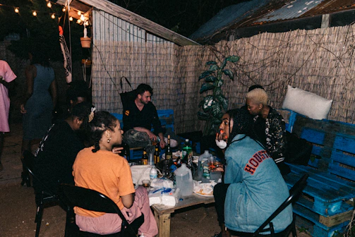 A group of friends gathered around a small table, sharing a signature bite and laughter under tech teal string lights.