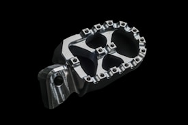 A close-up image of a metallic, machined part with a geometric design and bolts around the edges, placed against a black background.