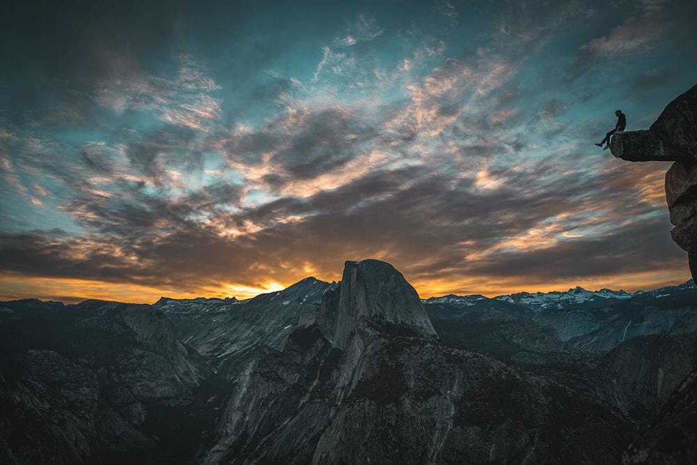 person sitting on edge rock mountain