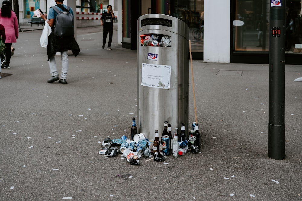 bottles beside public trash bin near people and building