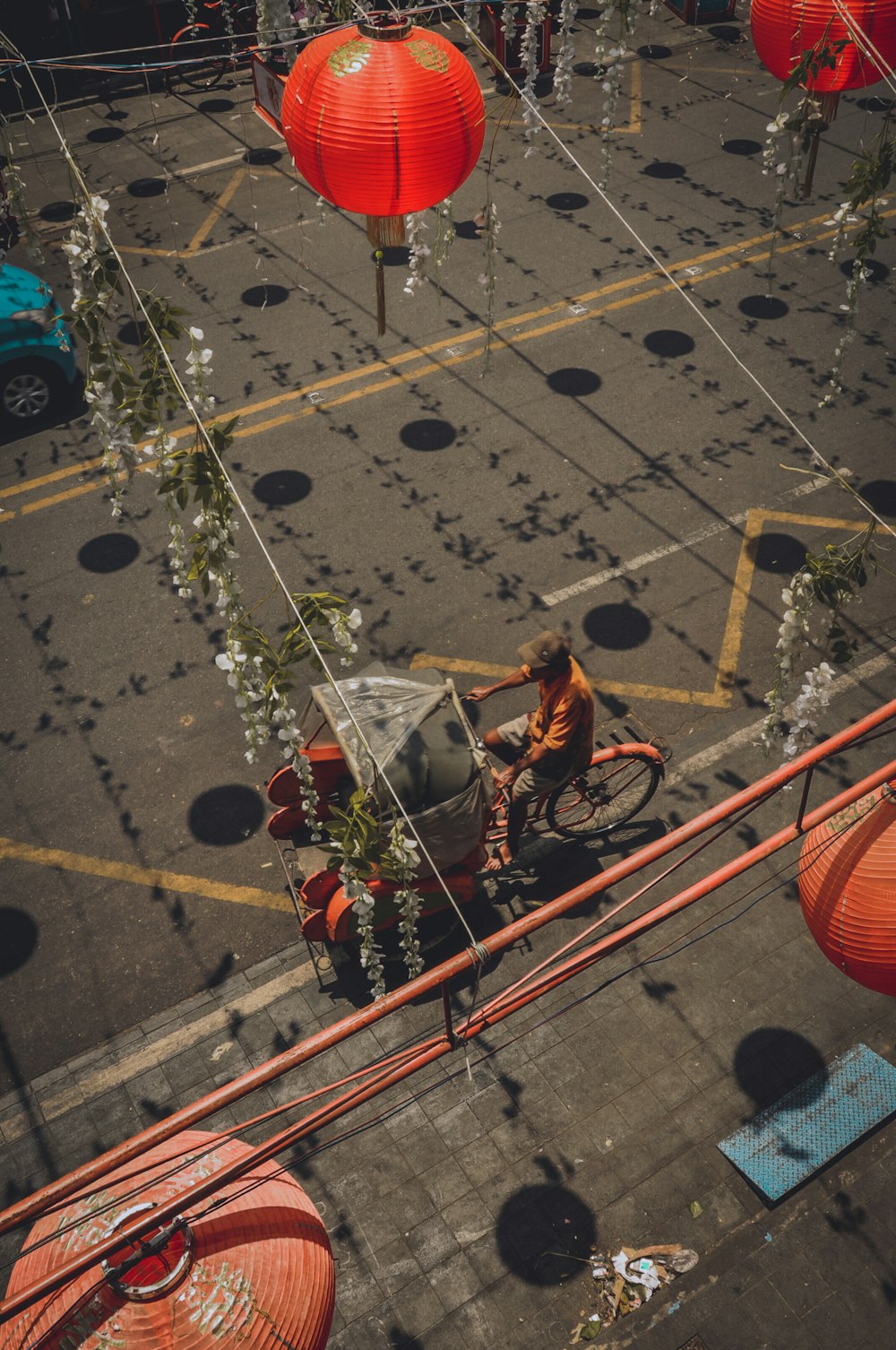 man riding bike with passenger canopy on road below Chinese lanterns